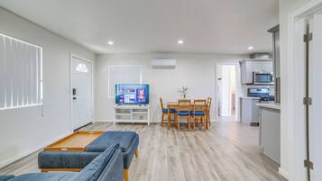 A modern living room with a sofa set, a TV, a dining table with chairs, and a kitchen area with appliances.