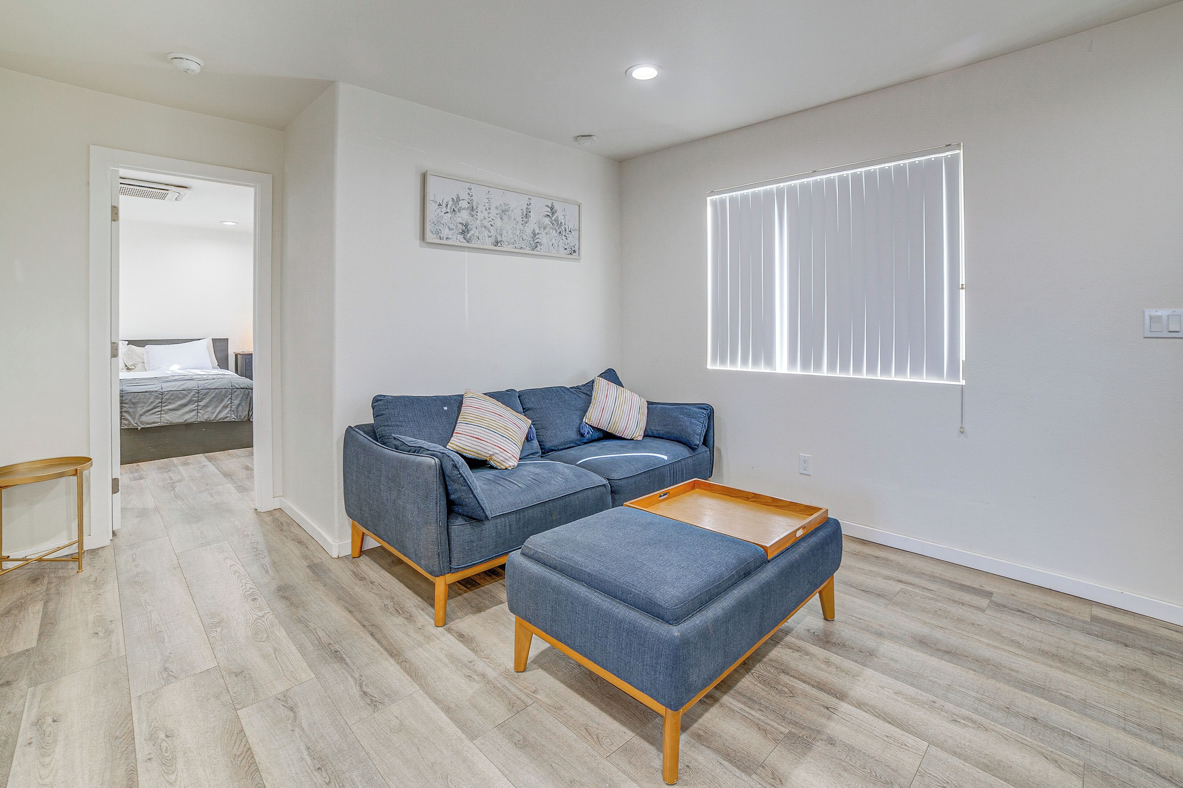 A modern living room with a sofa, ottoman, and a painting on the wall.