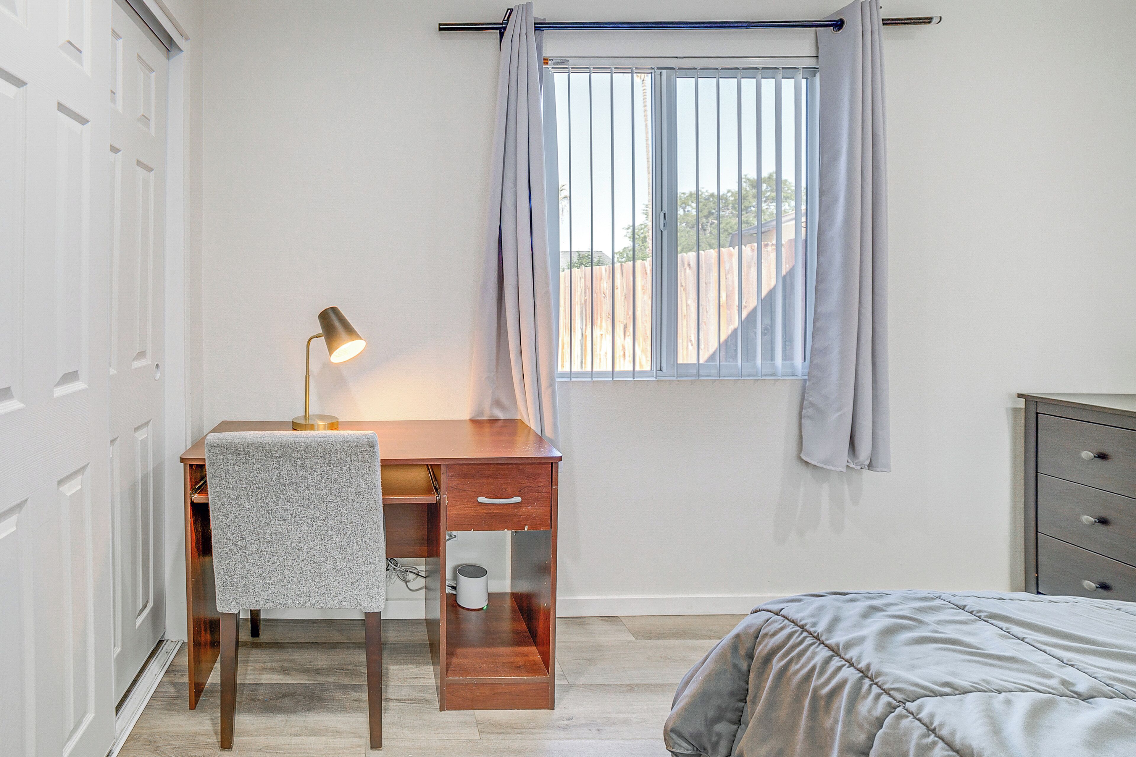 Een slaapkamer met een bed, een bureau met stoel, een raam met gordijnen en een radiator.