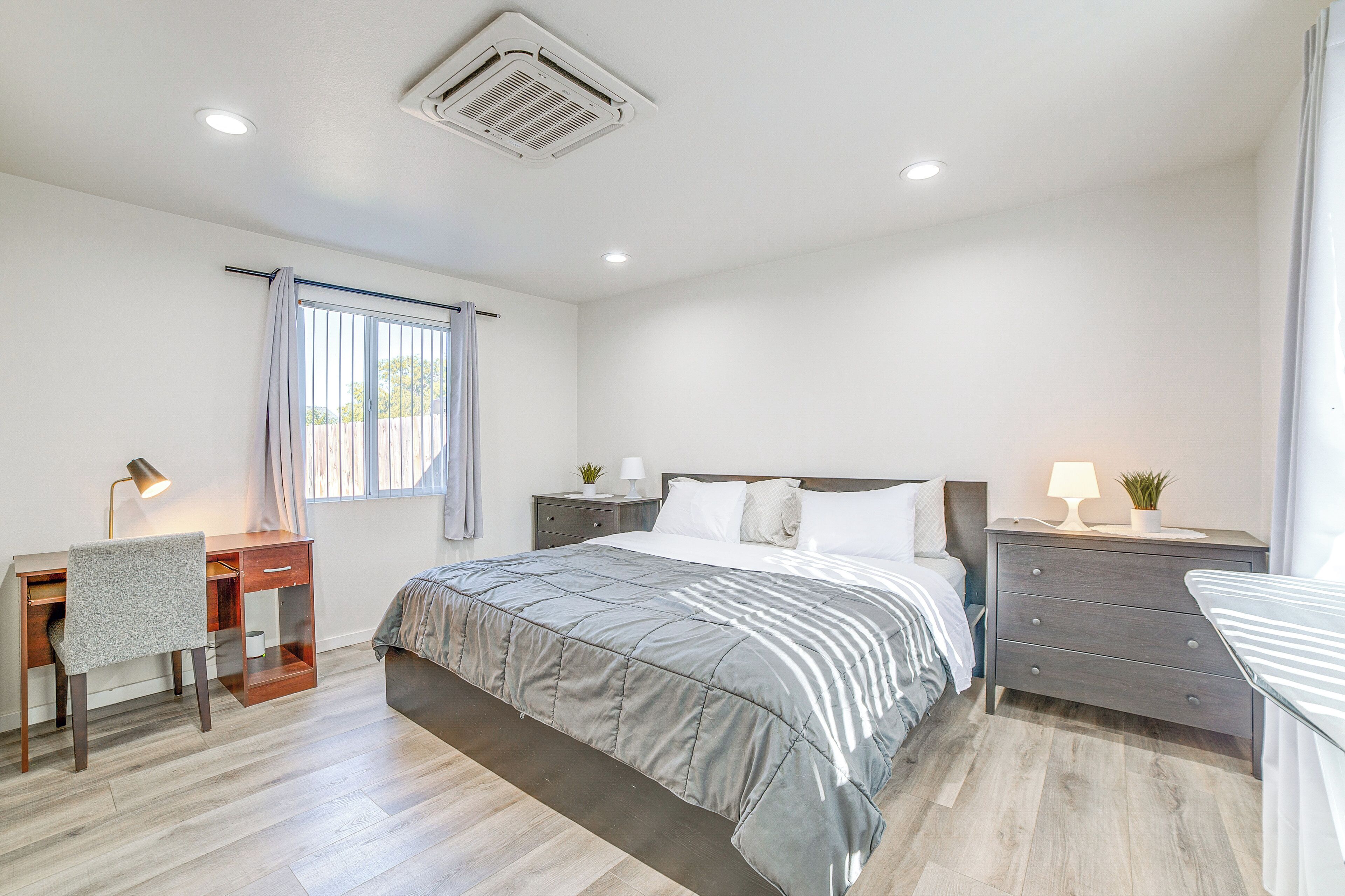Un dormitorio con cama, escritorio, cómoda y ventana con cortinas.