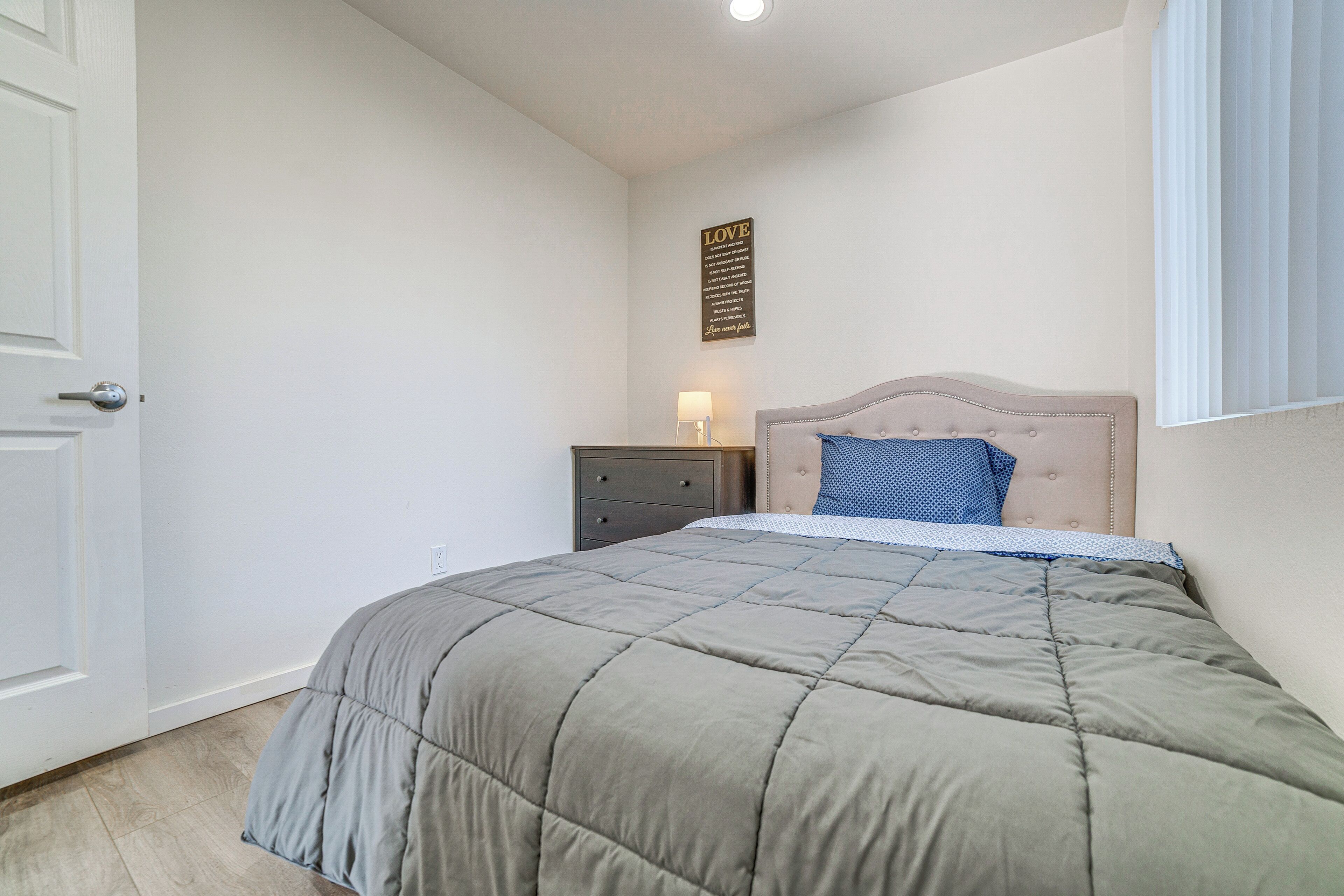 A bedroom with a bed, a nightstand, a wall-mounted lamp, and a door.