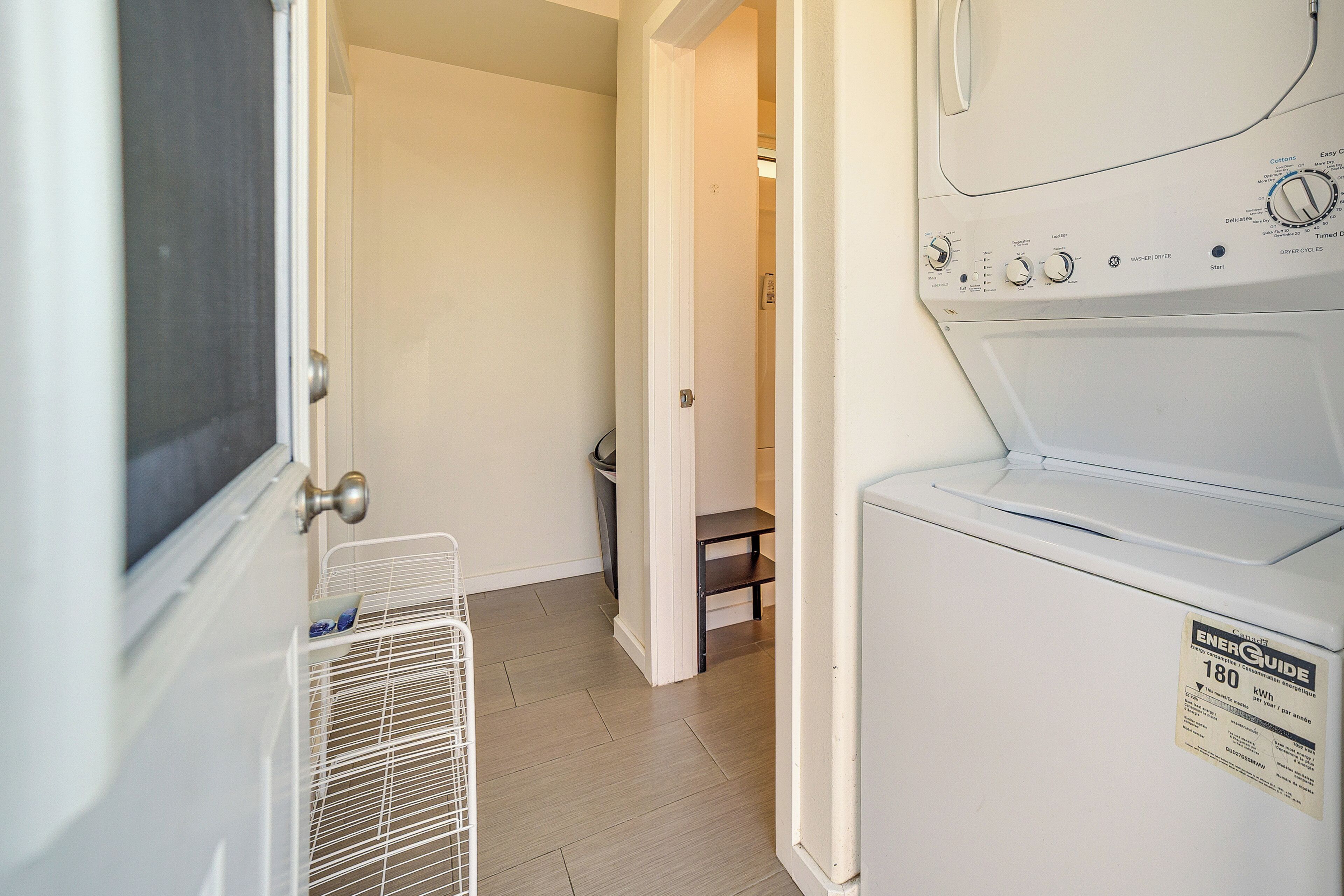 A laundry room with a white washer and dryer, a metal rack, and a door leading to another room.