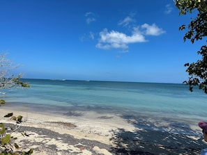 Ein Strand mit klarem Wasser, einem entfernten Boot und blauem Himmel.