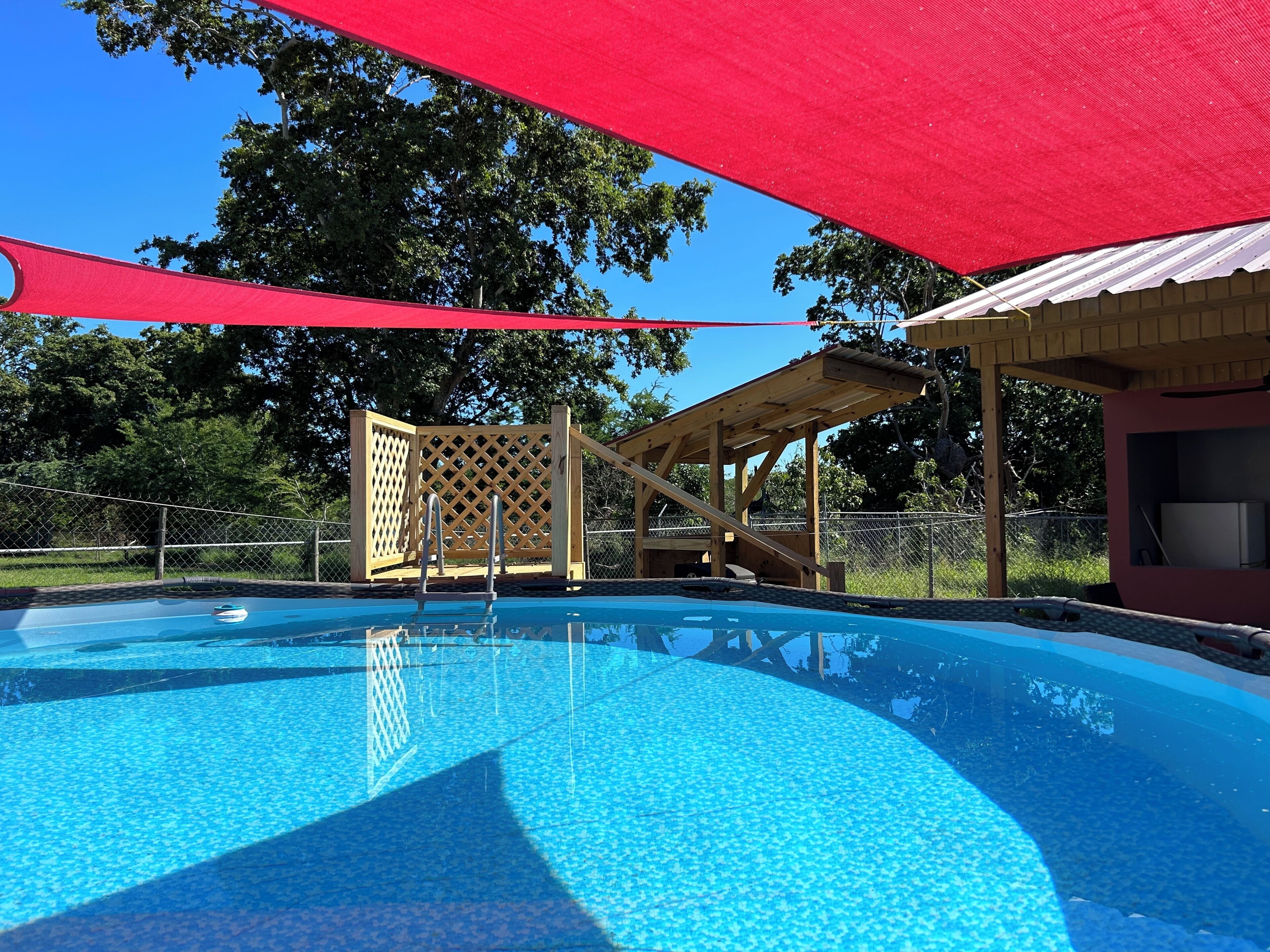 Une piscine avec une terrasse en bois et un espace salon abrité.