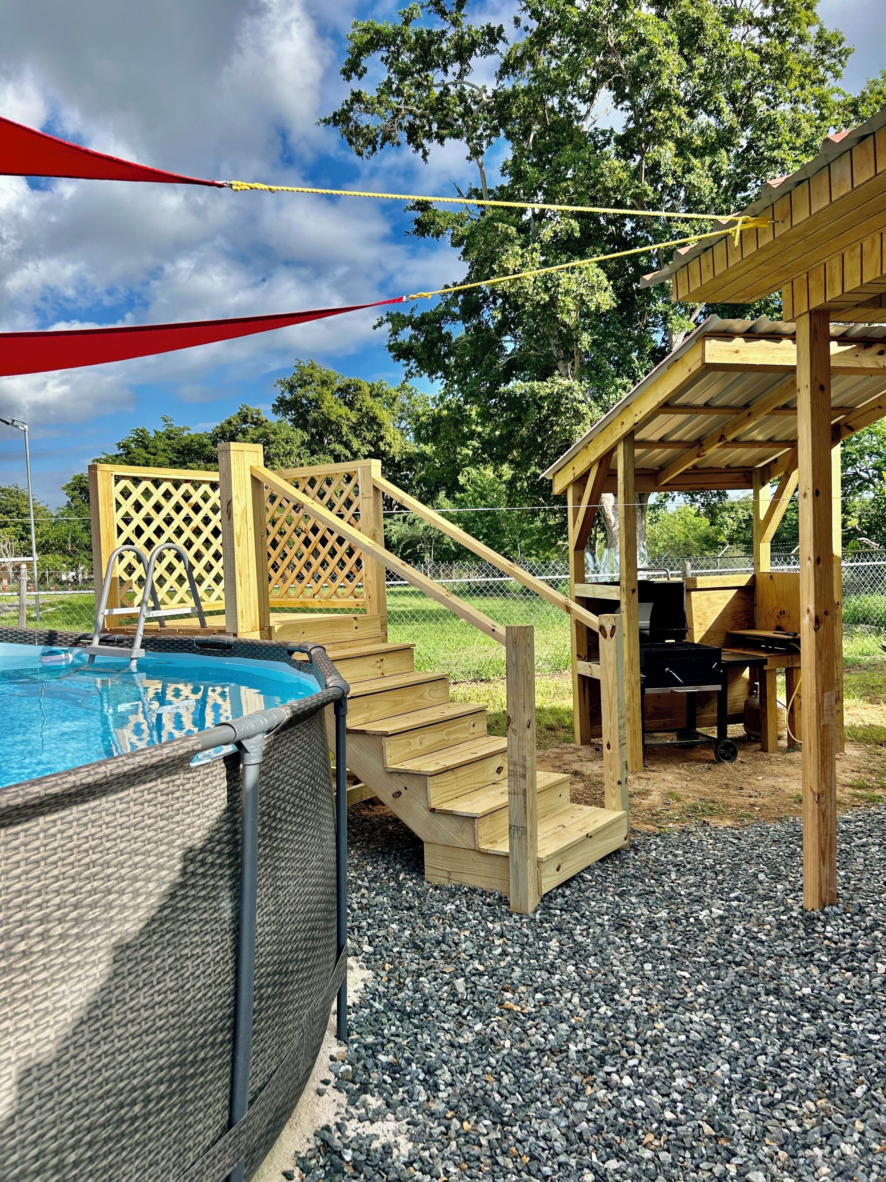 A wooden deck with a pool, a covered barbecue area, and a lattice fence.