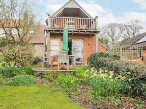 A two-story house with a balcony, a garden with daffodils, and a green umbrella. - Bell House Cottage (Craven Arms)