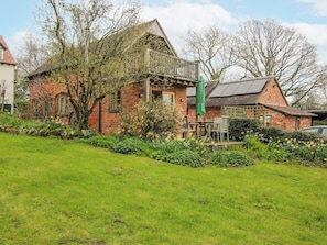 A brick house with a balcony, a garden with daffodils, and a green umbrella. - Bell House Cottage (Craven Arms)