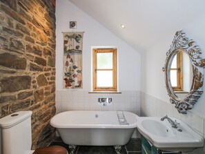 A bathroom with a stone wall, a bathtub, a sink, a mirror, and a window. - Bell House Cottage (Craven Arms)