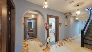 A hallway with a stone floor, wooden doorways, and a staircase. - Hotel Your Hive (Srinagar)