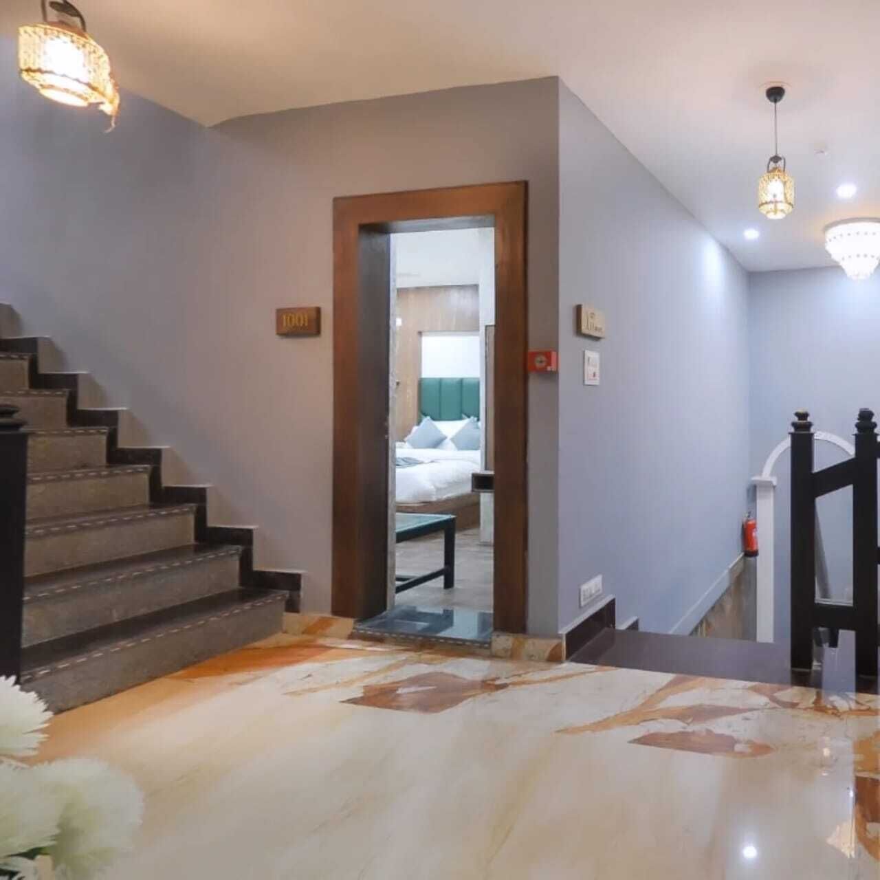 Habitación de hotel con piso de mármol, cama con cabecera verde, escalera de madera y una pequeña mesa.