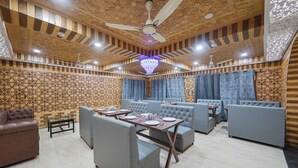 A restaurant with a patterned ceiling, ceiling fans, and blue curtains. - Hotel Your Hive (Srinagar)