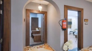 A hallway with a wooden floor, a fire extinguisher, and a mirror reflecting a room. - Hotel Your Hive (Srinagar)