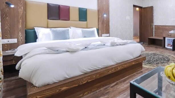 A modern hotel room with a wooden bed frame, a glass coffee table, and a view of the hallway. - Hotel Your Hive (Srinagar)