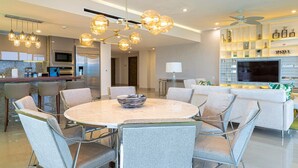 A modern kitchen with a built-in oven and microwave, a dining area with a marble table and grey upholstered chairs, and a living area with a sofa and a flat-screen TV. - Spacious 3-bedroom condo with AC in enchanting Cancún (Cancún)