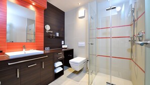 A modern bathroom with a large mirror, a sink, a toilet, and a glass-enclosed shower. - Double room Seeblick Deluxe (Heimbach)