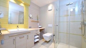 A modern bathroom with a glass shower enclosure, a large mirror, and a vanity with a sink and storage drawers. - Double room Seeblick Deluxe (Heimbach)