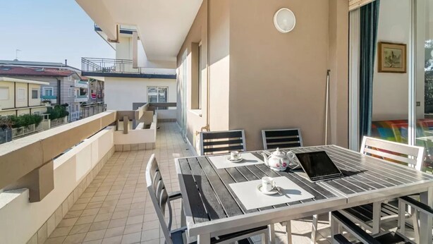 A balcony with a table set for two, a chair, and a window with a view of buildings. - GuestHost - Rimini Gelsomino Huge Apartment (Rimini)