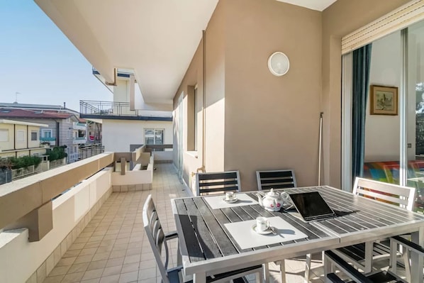 Ein Balkon mit Tisch für zwei Personen, einem Stuhl und einem Fenster mit Blick auf Gebäude.