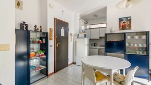 A compact kitchen with a dining area, white tiled floor, and a door with a note. - GuestHost - Rimini Gelsomino Huge Apartment (Rimini)