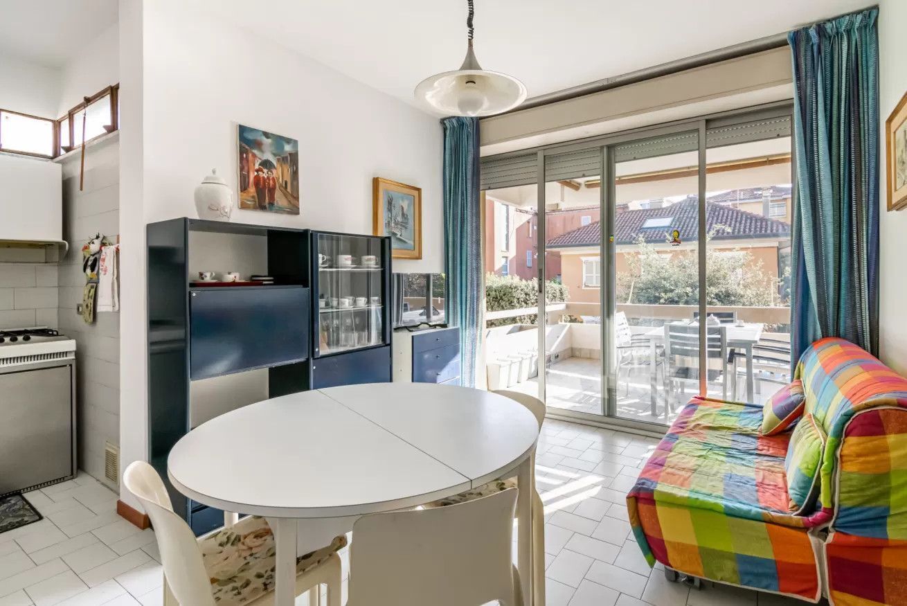 A modern kitchen with a dining table, a colorful sofa, and a large sliding glass door leading to an outdoor patio.