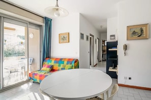 Ein Zimmer mit rundem Tisch, einem bunten Sofa, einem großen Fenster und einer Tür, die auf einen Balkon führt.