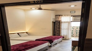 A hotel room with two beds, a ceiling fan, a clock, and a window with curtains. - Shri Ved Vrinda Dham Aashram (Vrindavan)