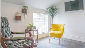 A living room with a large window, a television mounted on the wall, and two chairs.