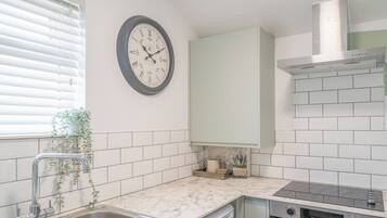 Une cuisine moderne avec des carreaux de céramique blancs disposés en motif métro, un évier en acier inoxydable, un four encastré et une horloge murale.