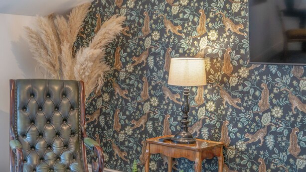 A tufted leather armchair, a small wooden side table with a lamp, and a decorative wall with a leopard print pattern.
