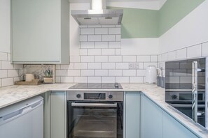 A kitchen with white subway tiles, a built-in oven, a stove, and a coffee machine.