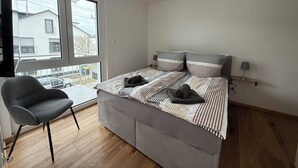 A bedroom with a bed, a chair, a desk, and large windows. - Simon Living - Apartment Pyramide central and quiet location in Karlsruhe (Karlsruhe)