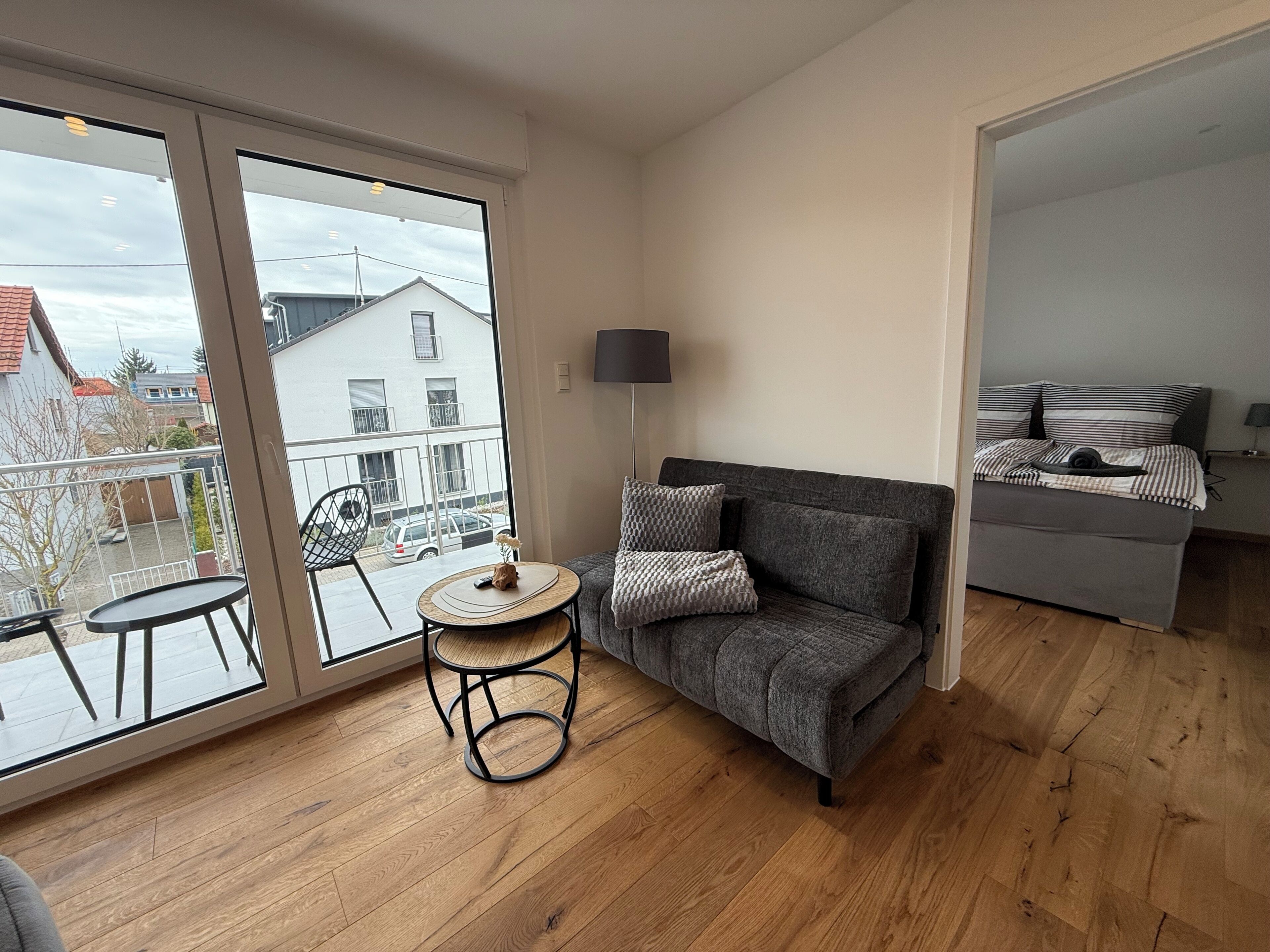 Ein modernes Wohnzimmer mit grauem Sofa, einem kleinen runden Tisch und Blick ins Freie.