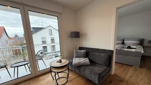 A modern living room with a grey sofa, a small round table, and a view of the outside. - Simon Living - Apartment Pyramide central and quiet location in Karlsruhe (Karlsruhe)