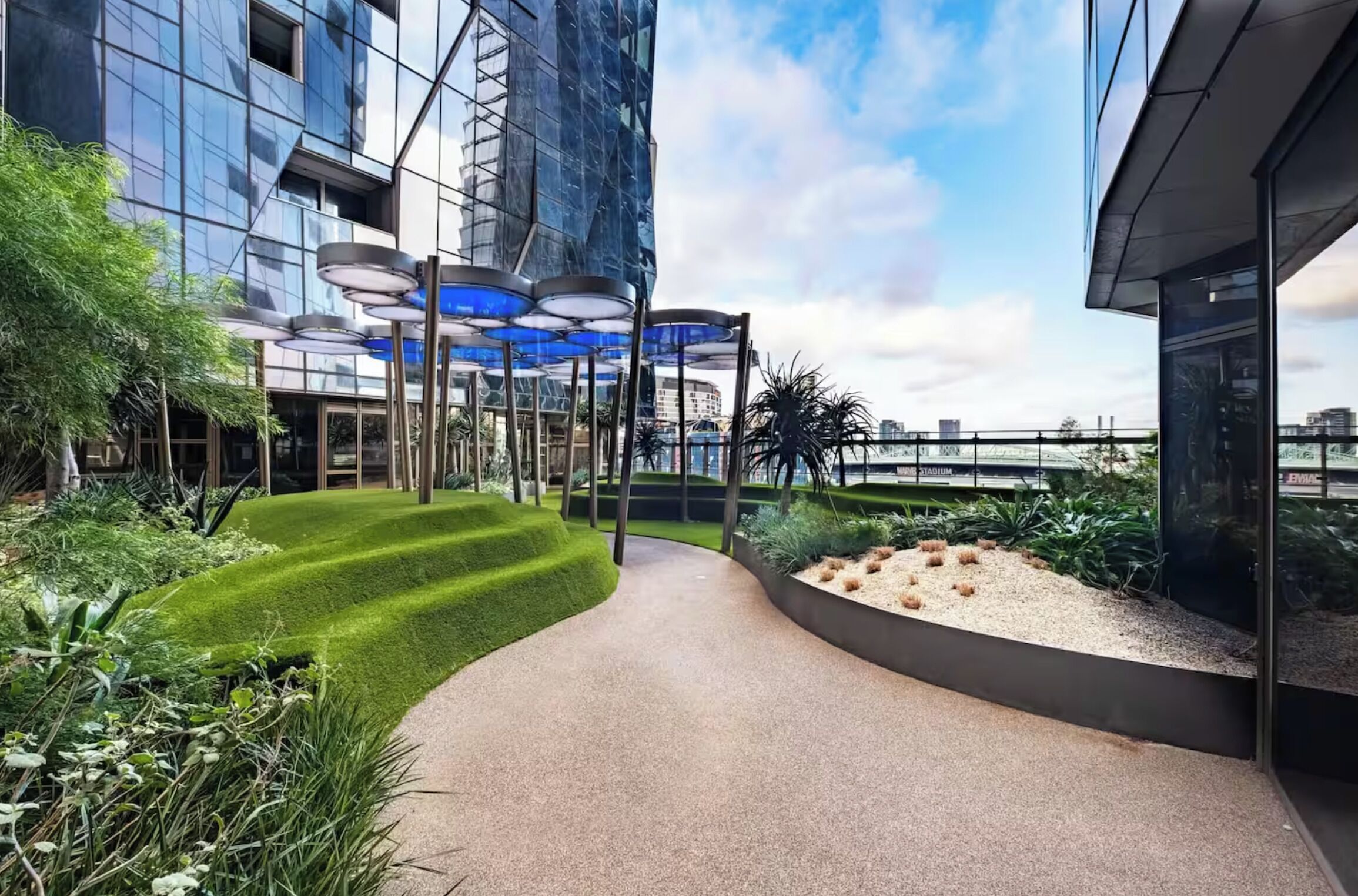 Un edificio moderno con finestre a vetro riflettente, un viale curvo e un'area giardino paesaggistica con erba verde e piante.