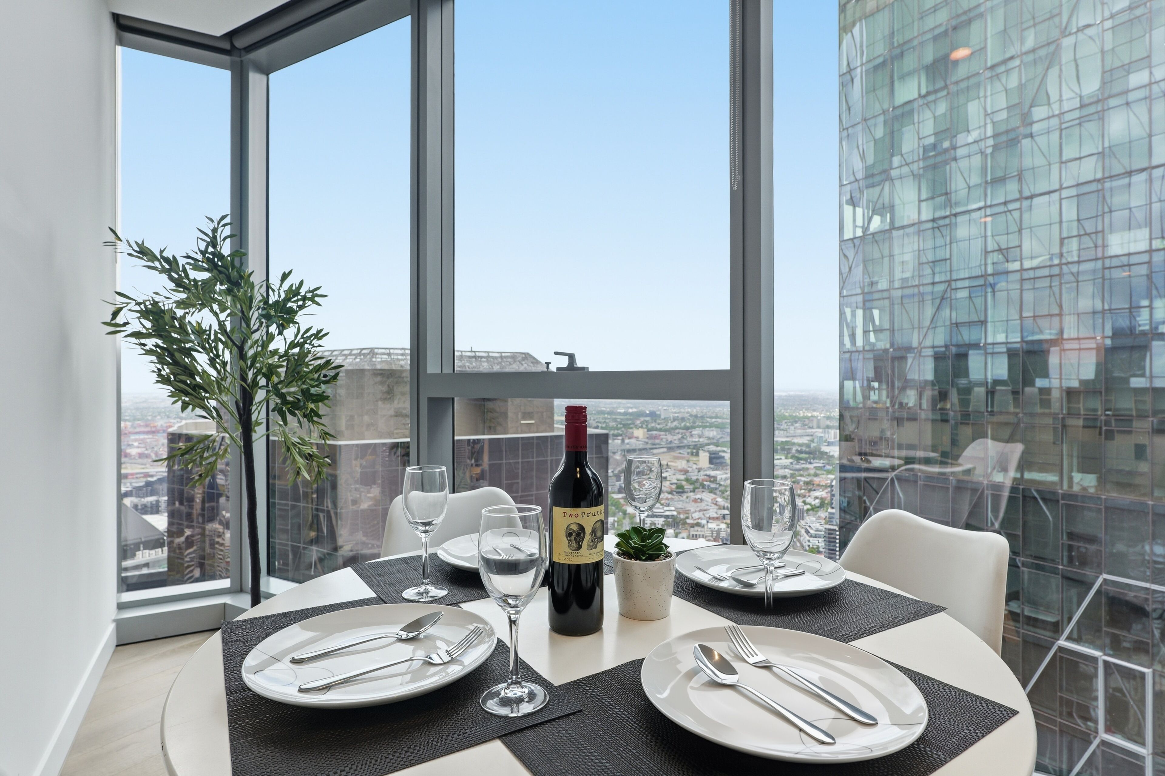 A dining table set with plates, cutlery, and wine glasses, with a bottle of wine and a small plant on the table.