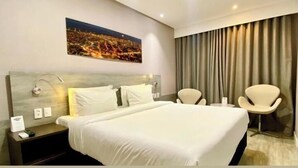 A hotel room with a bed, two chairs, a nightstand, a lamp, a painting, and a curtain. - NORD LUXXOR CITYMIX (Campina Grande)