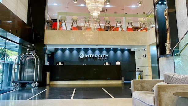 A hotel lobby with a reception desk, a chandelier, a luggage cart, and a seating area. - NORD LUXXOR CITYMIX (Campina Grande)