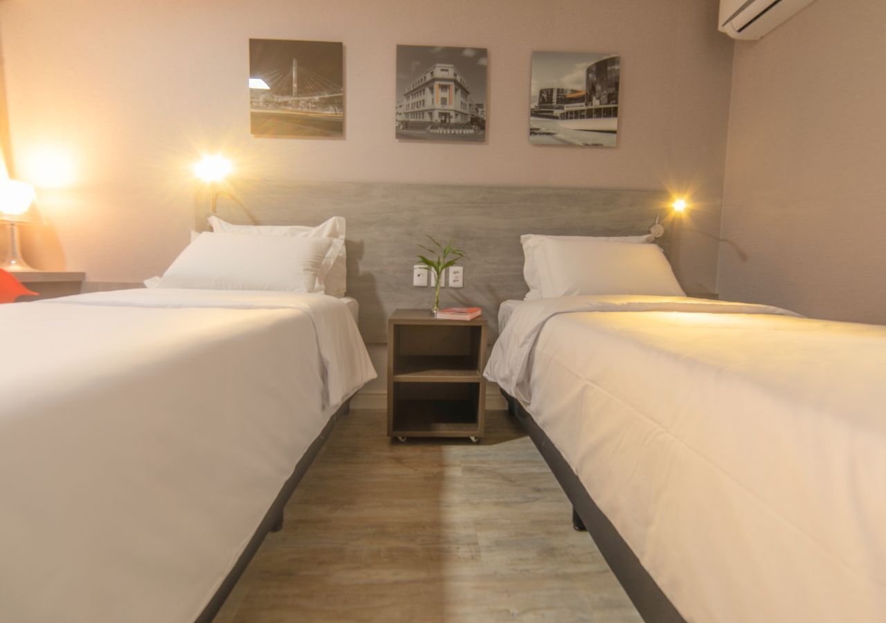 Habitación de hotel con dos camas, una mesita de noche con una planta y tres cuadros en la pared.