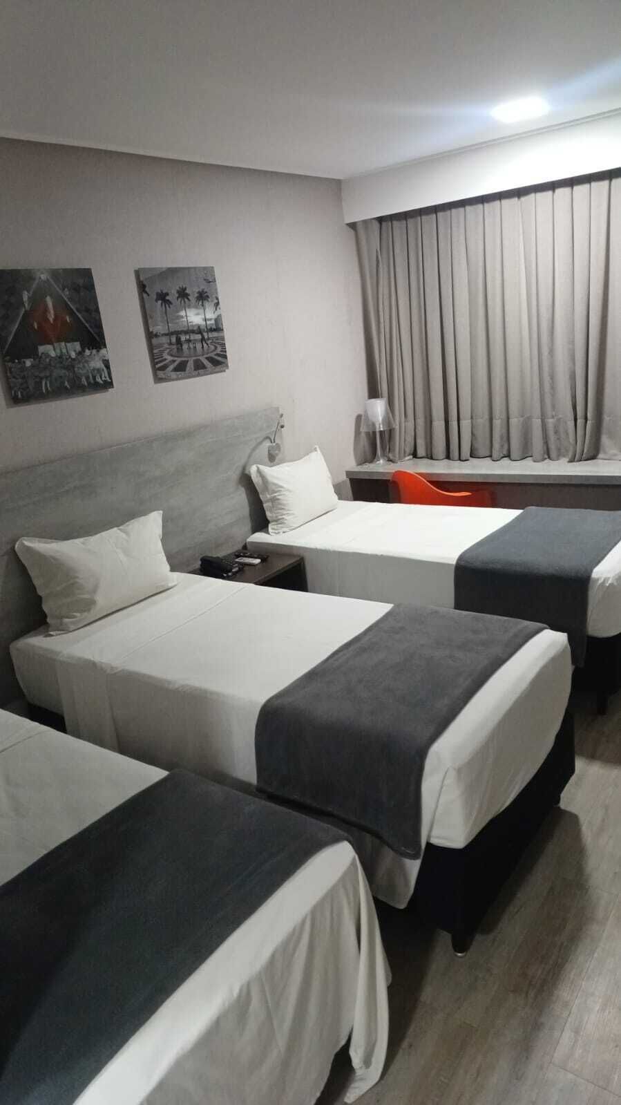 Ein Hotelzimmer mit drei Betten, einem Schreibtisch, einem Stuhl, einer Lampe und zwei Wandbildern.