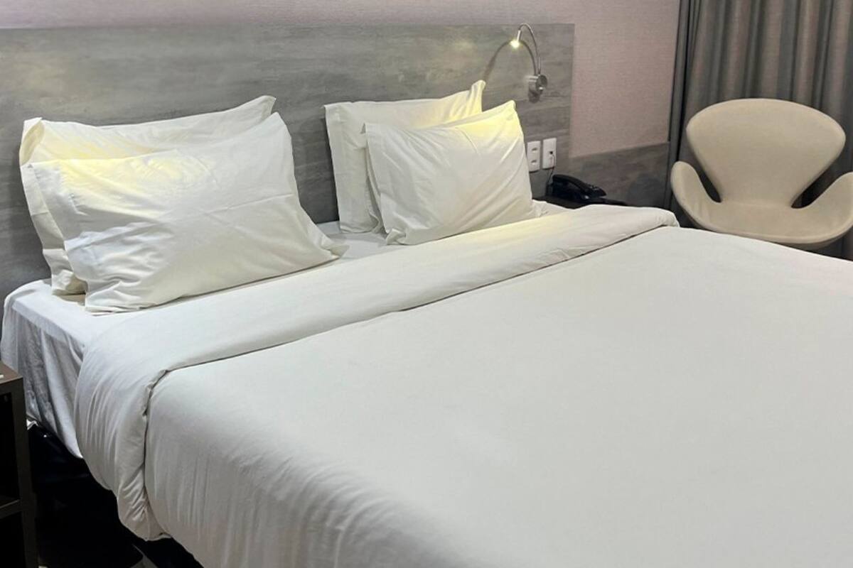Una habitación de hotel con una cama grande, dos almohadas, una lámpara de noche, una silla y un aplique en la pared.