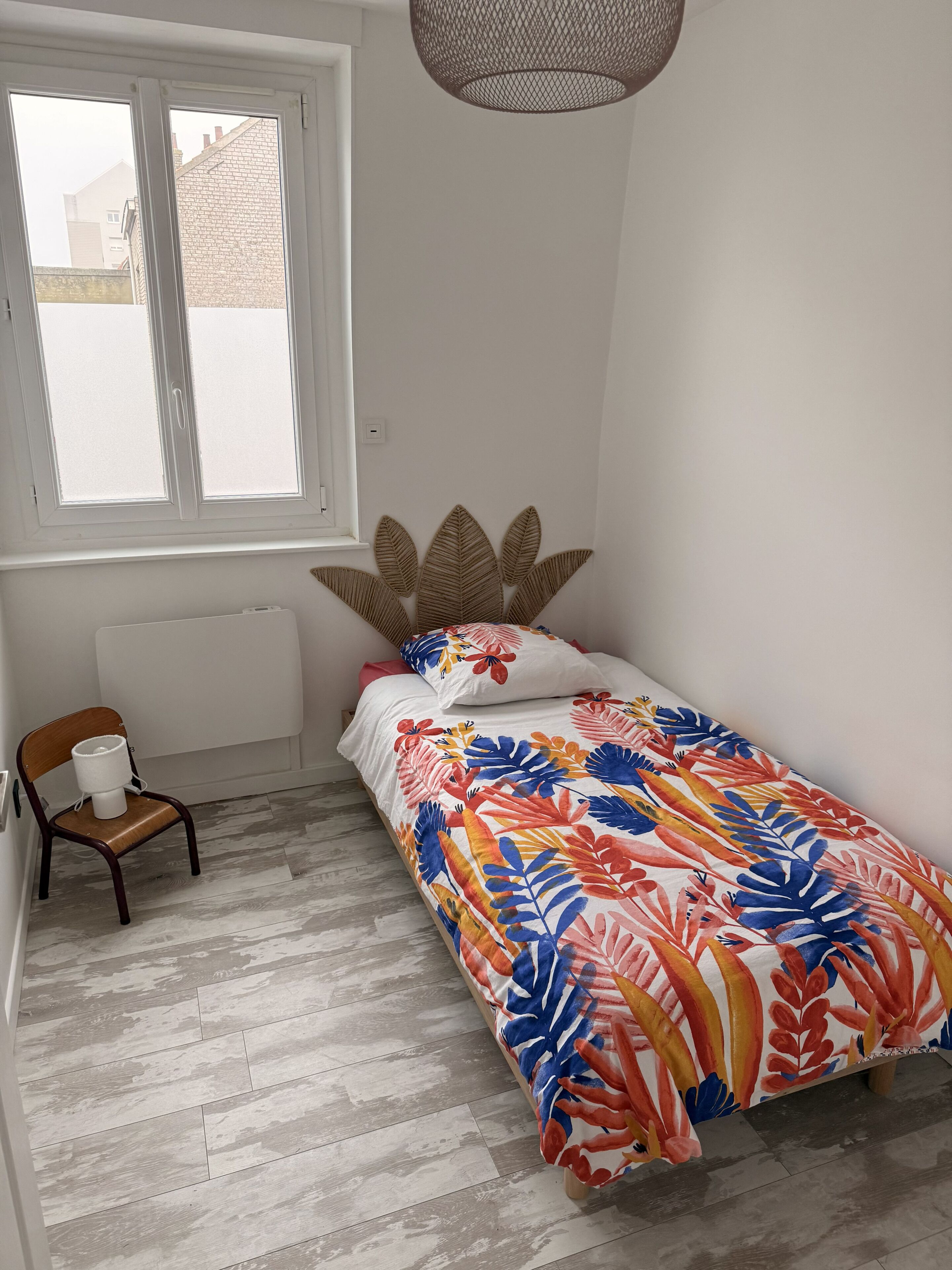 A bedroom with a bed, a chair, a radiator, and a window.