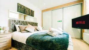 A hotel room with a bed, a television displaying 'NETFLIX,' a sliding door, and a wall-mounted artwork. - LUX Bloomsbury Flat By Holborn Covent Garden (London)