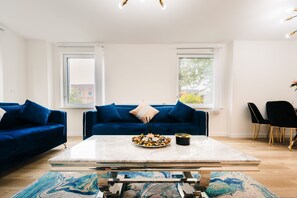 A modern living room with a blue sofa set, a marble coffee table, and a dining area with black chairs. - LUX Riverside Duplex Masionette By LCY Excel (London)