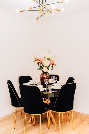 A dining table with black chairs, a vase of flowers, and a modern chandelier. - LUX Riverside Duplex Masionette By LCY Excel (London)