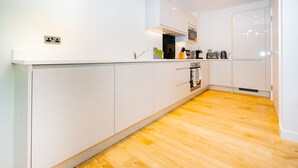 A modern kitchen with white cabinets, a wooden floor, and a built-in oven. - LUX Riverside Duplex Masionette By LCY Excel (London)