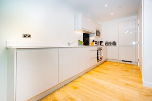 A modern kitchen with white cabinets, a wooden floor, and a built-in oven. - LUX Riverside Duplex Masionette By LCY Excel (London)