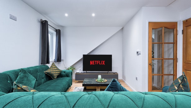 Ein Wohnzimmer mit einem grünen Sofa, einem Flachbildfernseher und einer Holztür.