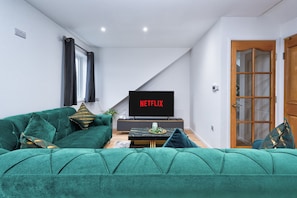 A living room with a green sofa, a flat-screen TV, and a wooden door. - Stylish Dagenham Flat Easy Central London Access (Dagenham)