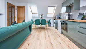 Eine moderne Küche mit Dachfenstern, ein Essbereich mit einem grünen Sofa und einem eingebauten Ofen.