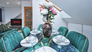 Ein Essbereich mit türkisfarbenen Polsterstühlen, einem Tisch gedeckt mit Tellern, Gläsern und einer Vase mit Blumen.